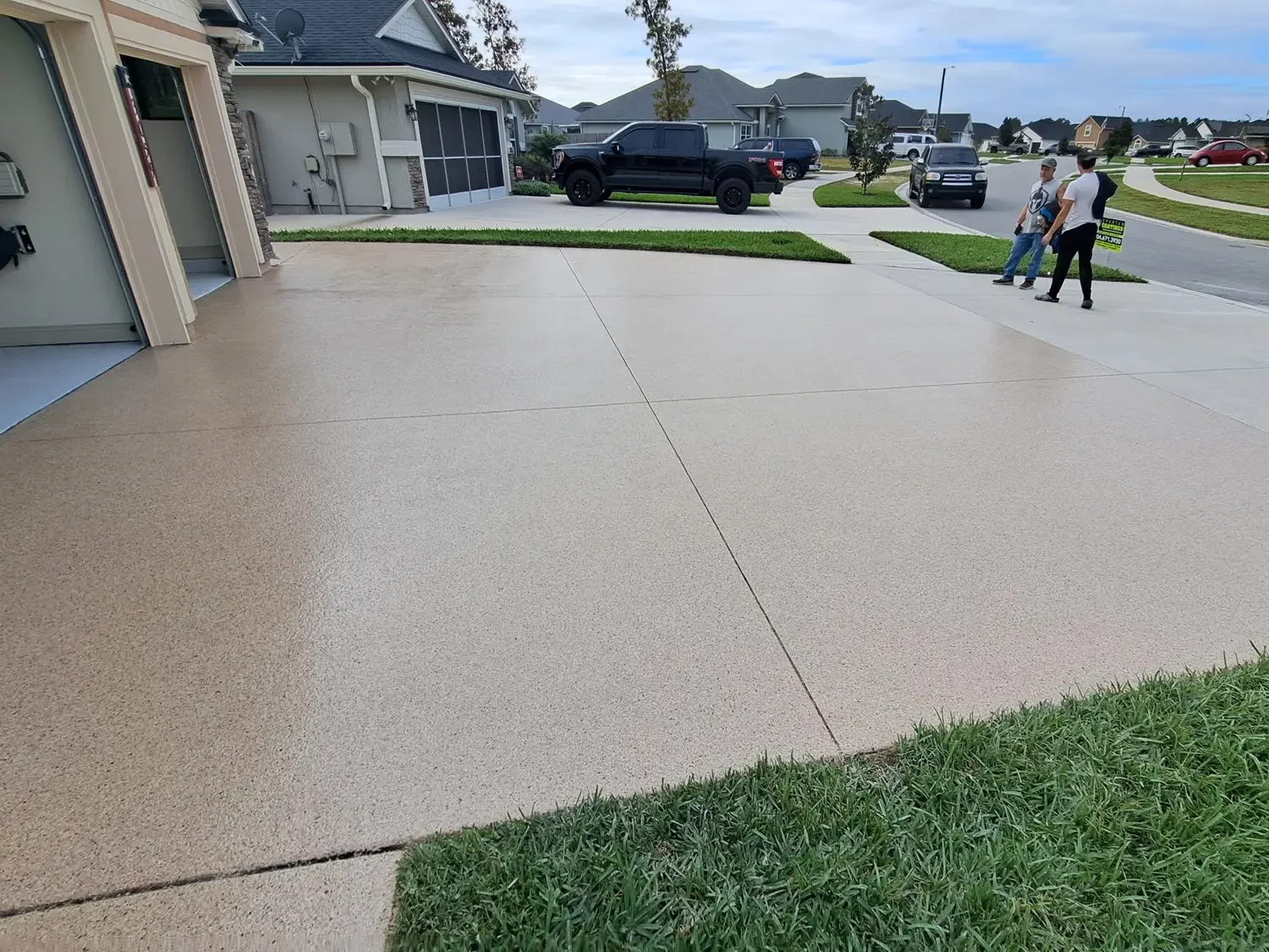 Tan flake coating across a two-car driveway with the subdivision street behind