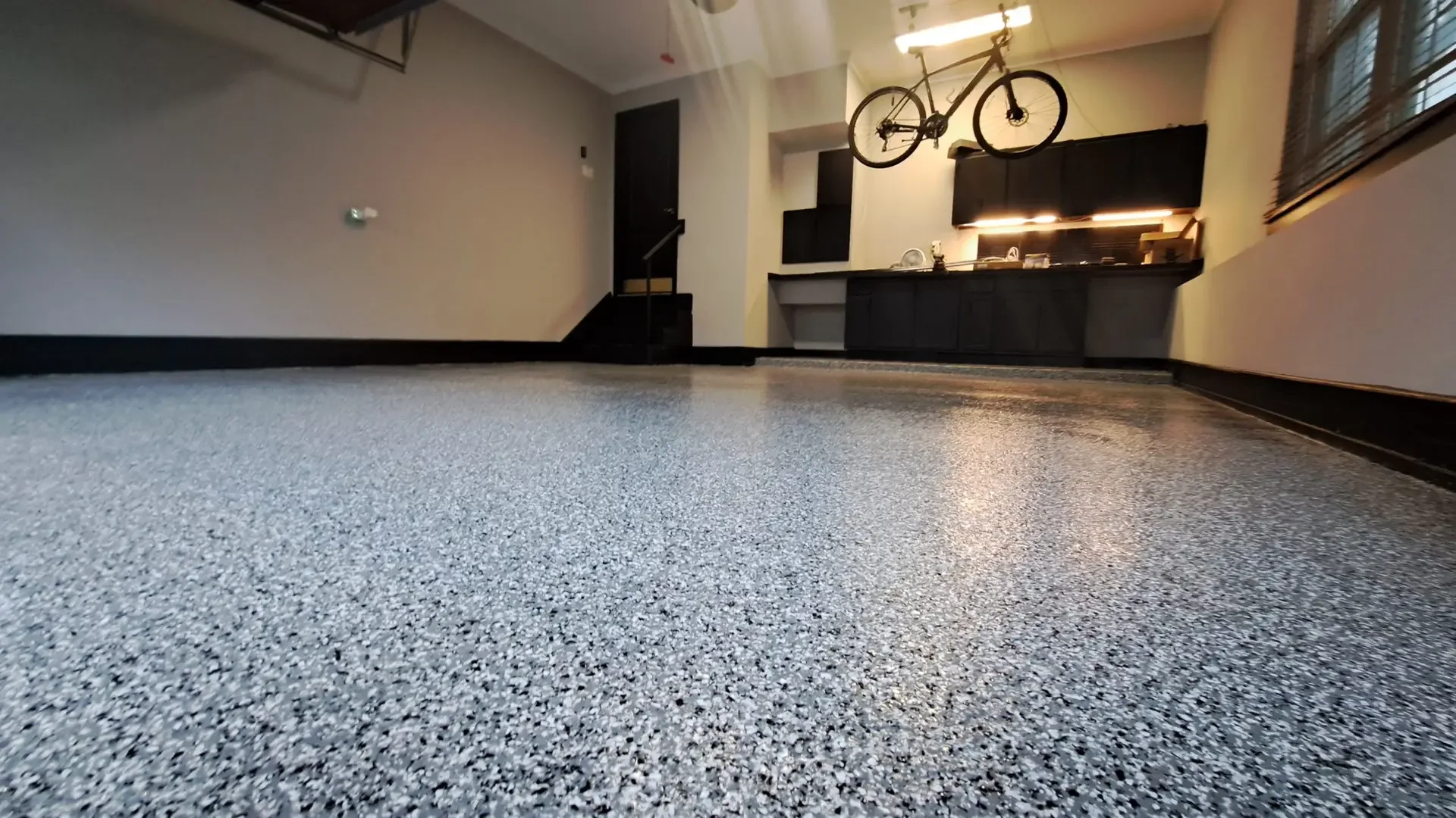 Gray and black flake epoxy floor in a garage with a bar, cabinets and a bike on the wall