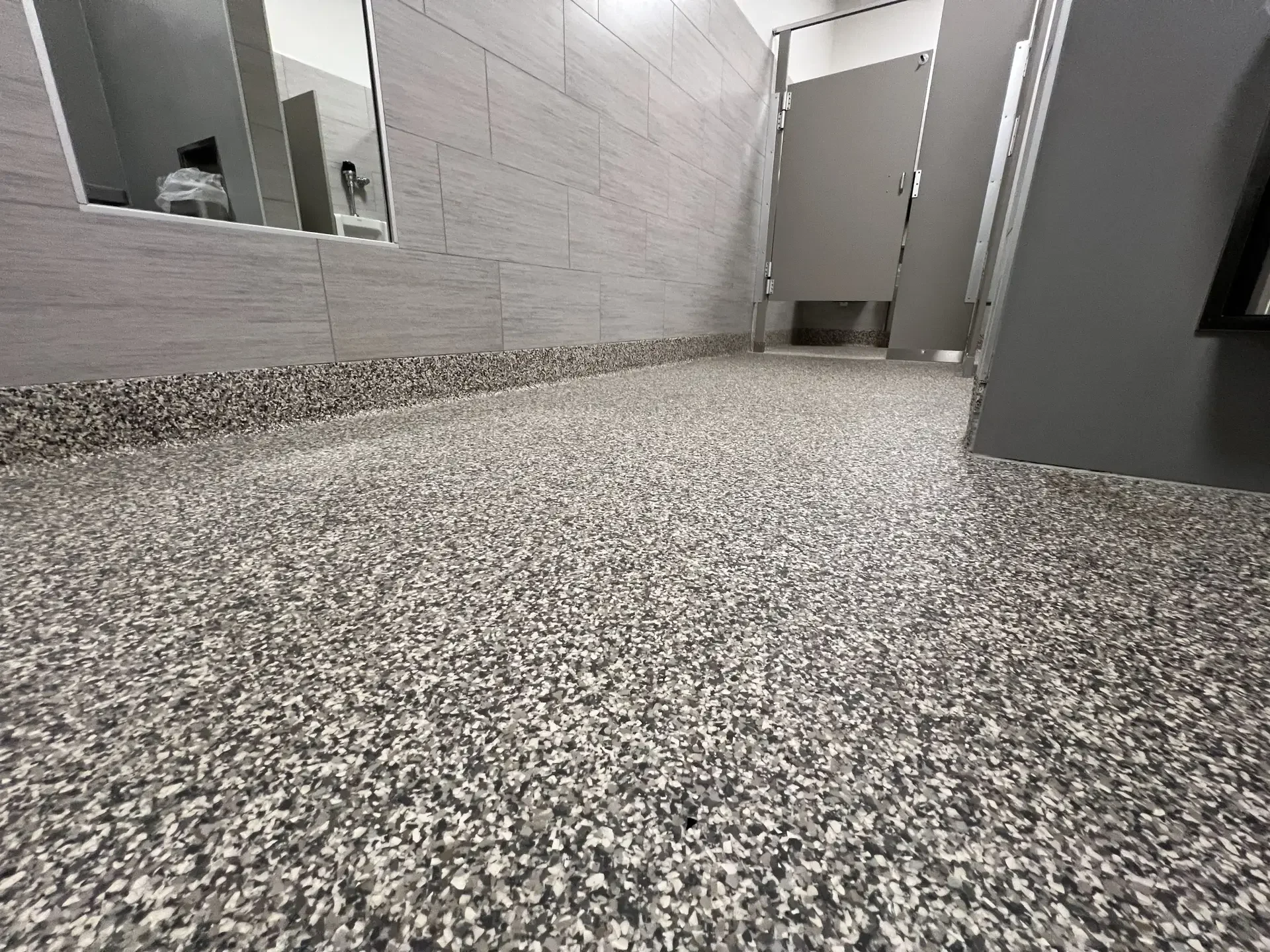 Gray flake epoxy floor in a commercial restroom corridor with partition doors