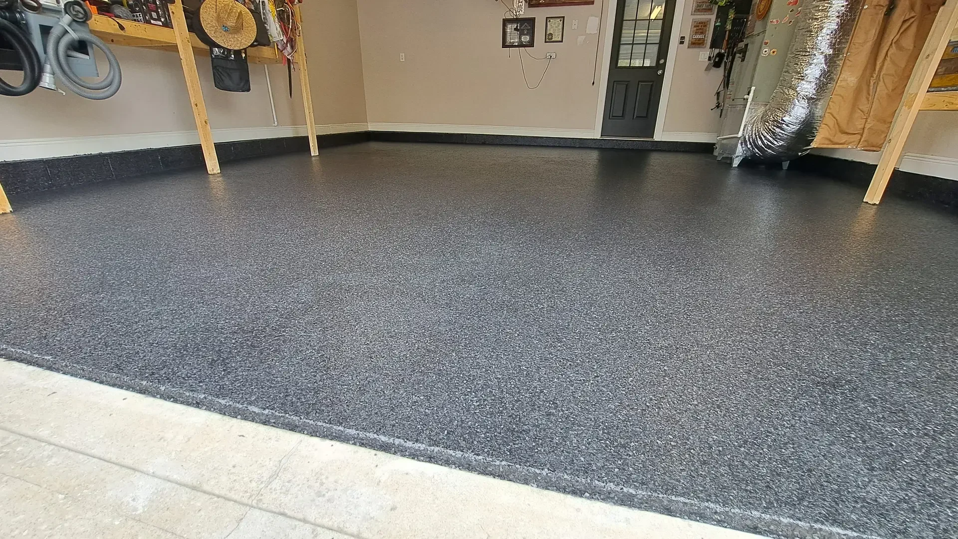 Dark flake epoxy garage floor with a black cove base and tools on the wall