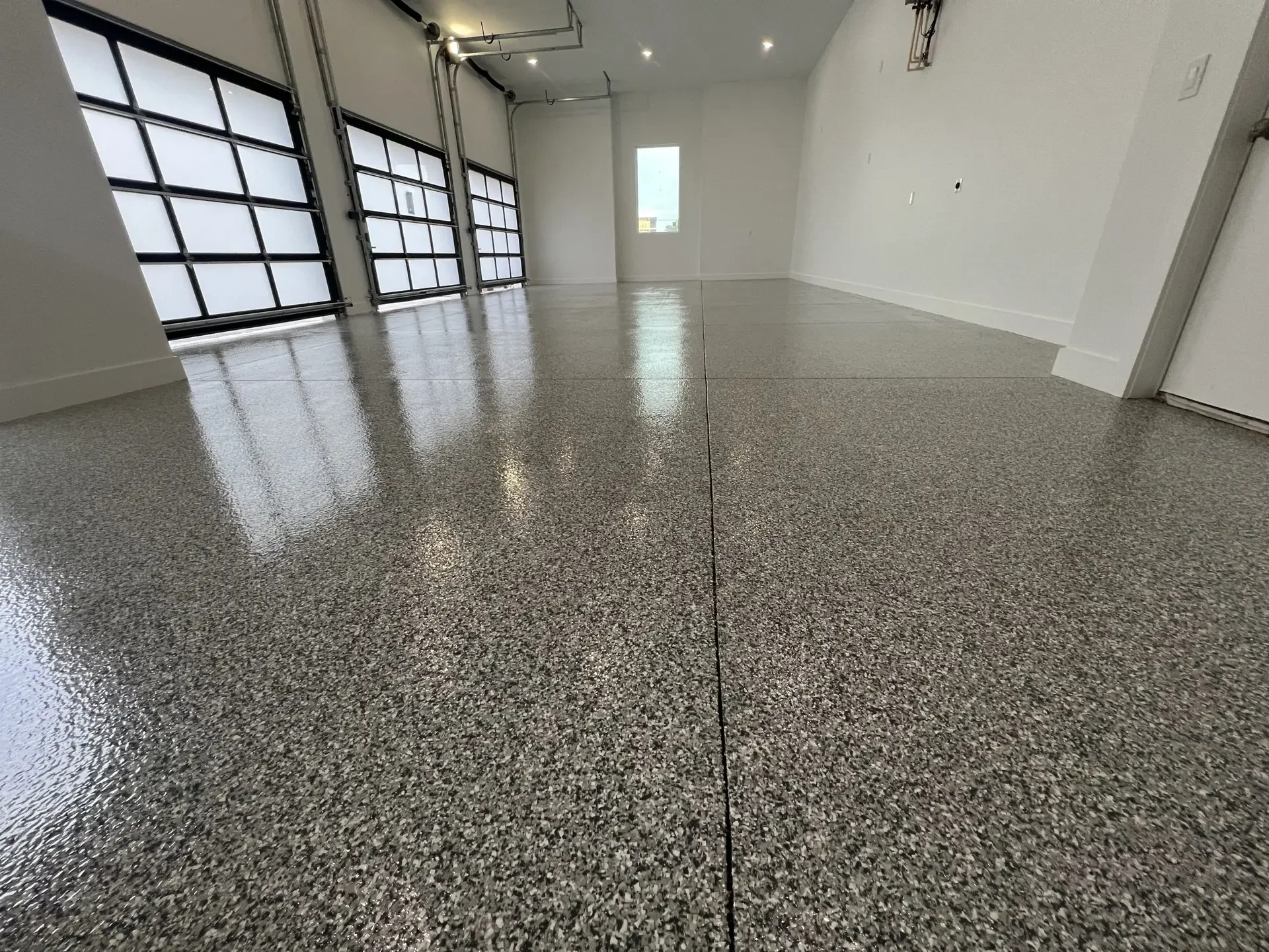 Glossy gray flake epoxy floor in a three-bay garage with glass garage doors