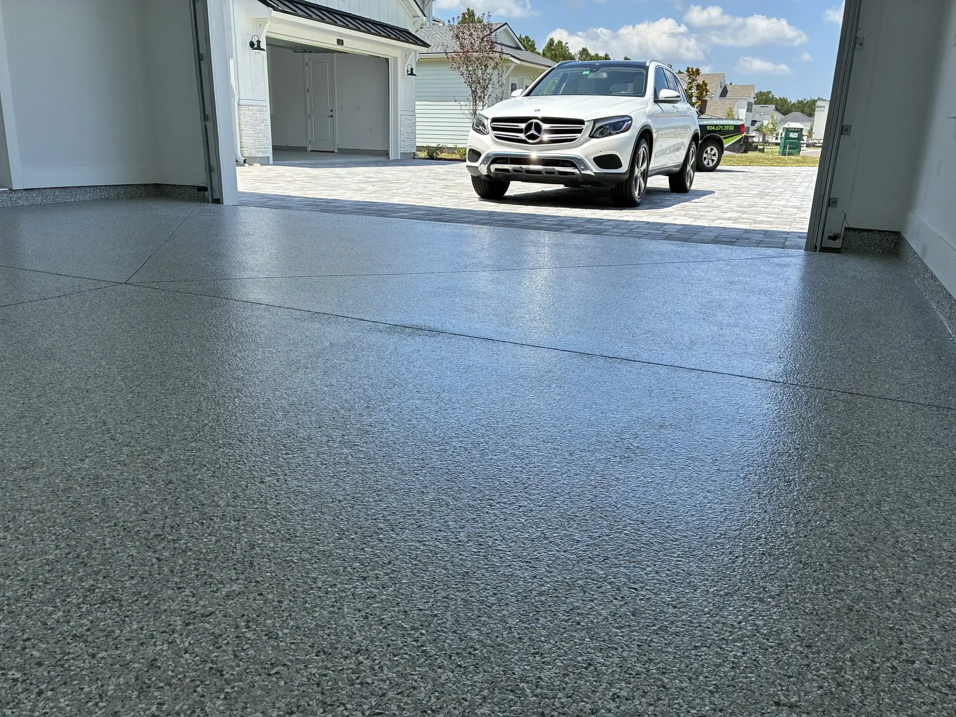 Salt and pepper flake epoxy garage floor looking out to a white SUV on a paver driveway