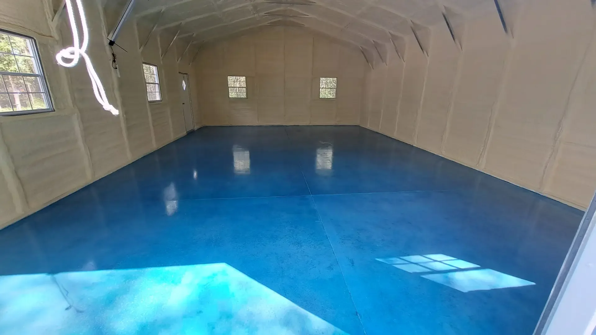 Blue metallic epoxy floor in a detached garage room with open trusses