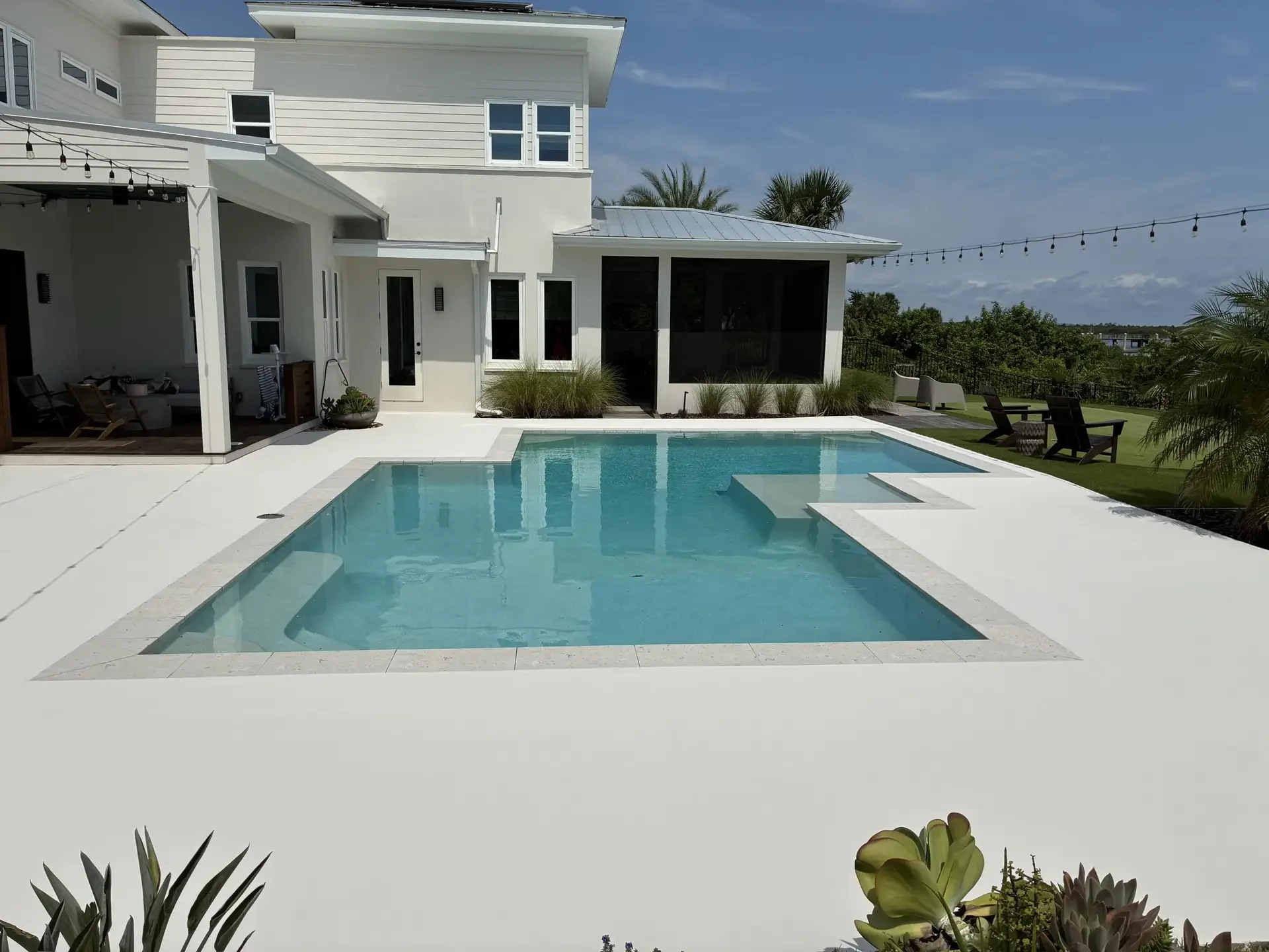 Bright white coated pool deck around a rectangular pool behind a two-story house